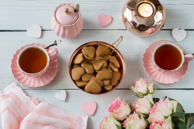 su un tavolo bianco rose rosa, tè in tazze rosa, torte, caramelle, decorazioni cuori di tessuto, zucchero