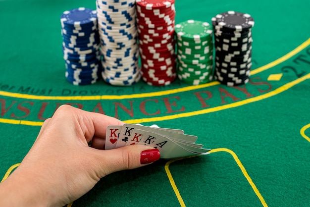 Su un tavolo da poker verde ci sono fiches colorate una sopra l'altra e una mano femminile tiene delle carte. Concetto di poker
