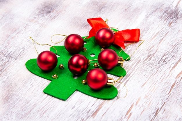 Su un tavolo di legno giace un albero di Natale in feltro fatto a mano con palline rosse e un fiocco rosso in alto