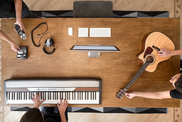 Su un tavolo di legno in uno studio di registrazione, una tastiera musicale, una chitarra acustica, un mixer audio e un computer.