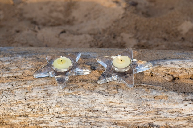 su un tronco nella sabbia ci sono due candelabri con una candela a forma di stella
