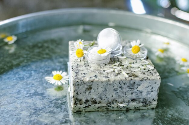 Su una lattina di crema di pietra di granito attorno ai fiori di camomilla freschi