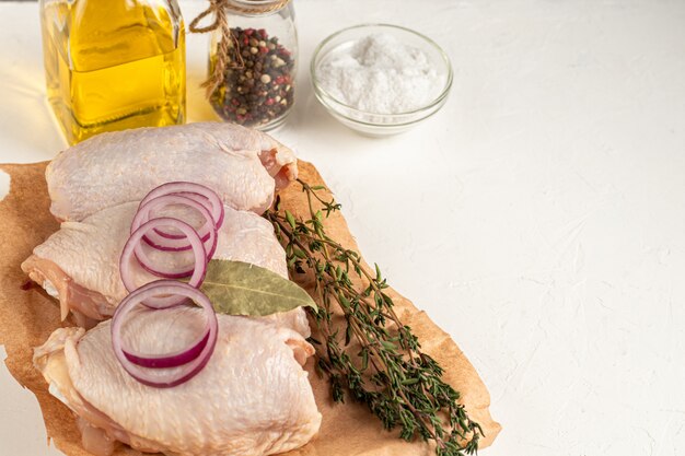 Su una tavola di legno, cosce di pollo senza pelle, accanto ai funghi, con pomodori, cipolle rosse e timo. Ricetta del piatto. Ingredienti. Su sfondo bianco