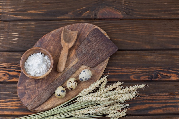 su una tavola di legno una spatola, un cucchiaio, una ciotola con farina, uova