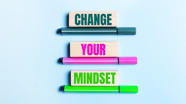 Su uno sfondo azzurro, ci sono tre pennarelli multicolori e blocchi di legno con la scritta CHANGE YOUR MINDSET