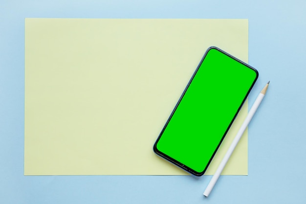Su uno sfondo blu un foglio di carta bianco un telefono con uno schermo verde e una matita