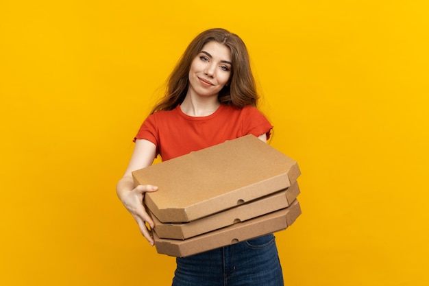 Su uno sfondo giallo brillante una donna che abbatte una maglietta cremisi di un servizio di consegna di pizza stringe alcune scatole di pizza ben pronte a fare una consegna