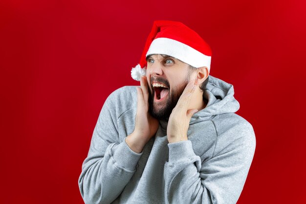 Su uno sfondo giallo di Natale, un uomo con una camicia rossa e un cappello di Babbo Natale è in piedi, con in mano i giocattoli di Capodanno di palline dorate davanti al viso