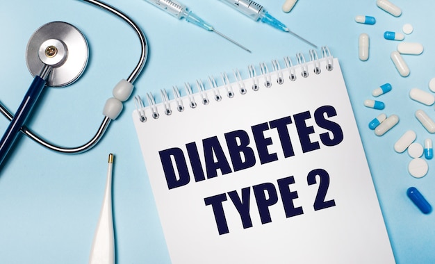 Su uno sfondo grigio chiaro, uno stetoscopio, un termometro elettronico, pillole, siringhe e un taccuino con il testo DIABETE TIPO 2. Concetto medico.