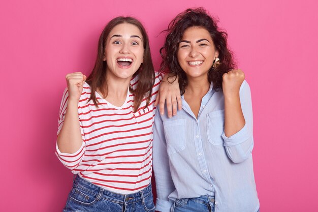 Successo. Donne caucasiche che sollevano le loro mani nello stupore felice isolato sopra il rosa