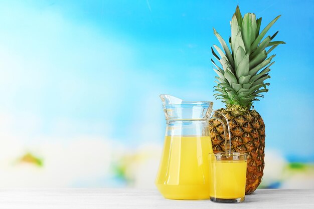 Succo d'ananas fresco in vetro e brocca su sfondo blu