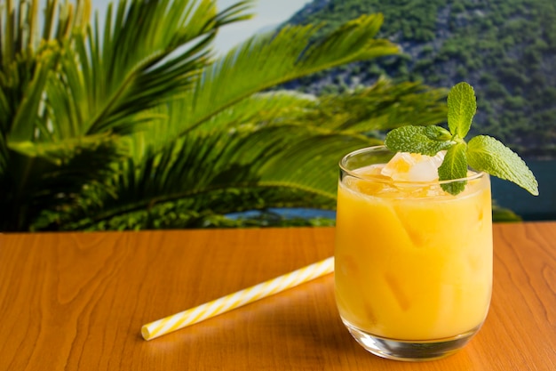 Succo d'arancia con ghiaccio nel bicchiere sul tavolo di legno sullo sfondo tropicale. Avvicinamento.