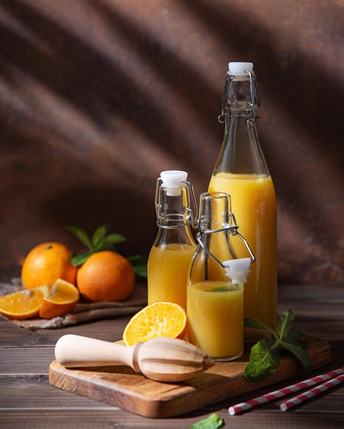 Succo d'arancia fresco fatto in casa in tre bottiglie con agrumi sul tagliere con ombre mattutine su uno sfondo di legno marrone. Vista frontale e copia dell'immagine dello spazio