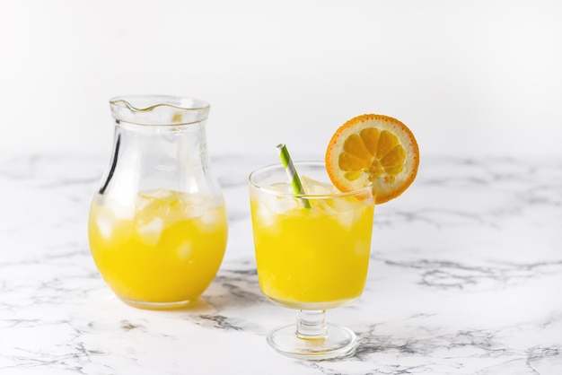 Succo d'arancia gustoso in vetro con cubetto di ghiaccio sfondo blu e bianco Arance fresche in orizzontale