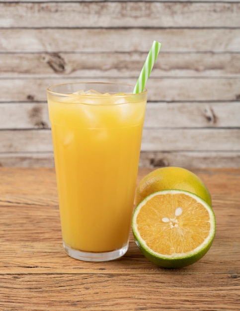 Succo d'arancia in un bicchiere con ghiaccio e frutta su un tavolo di legno.