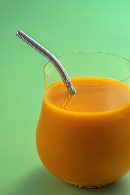 Succo d'arancia in un bicchiere con una cannuccia su sfondo verde