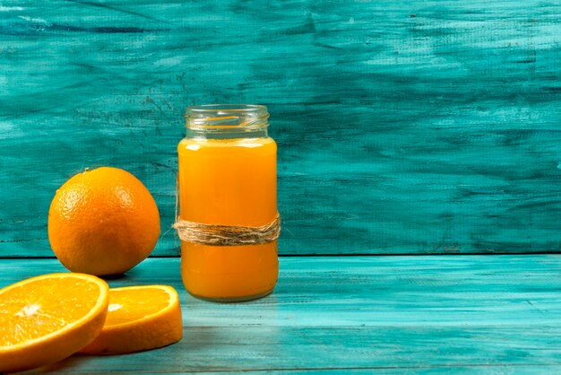 Succo d'arancia in vetro con fette d'arancia e ghiaccio su sfondo blu.
