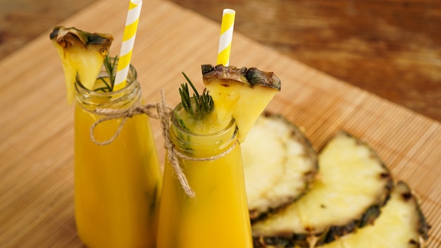 Succo di ananas fatto fresco con ghiaccio in una piccola bottiglia di vetro su fondo di legno. Bevanda fatta in casa.