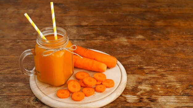 Succo di carota arancione brillante in un barattolo di vetro su uno sfondo di legno. Succo e carote tritate. Bevanda fatta in casa con vitamine