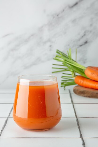 Succo di carota fresco in vetro sul tavolo e sfondo chiaro con carota fresca sul ponte di legno.