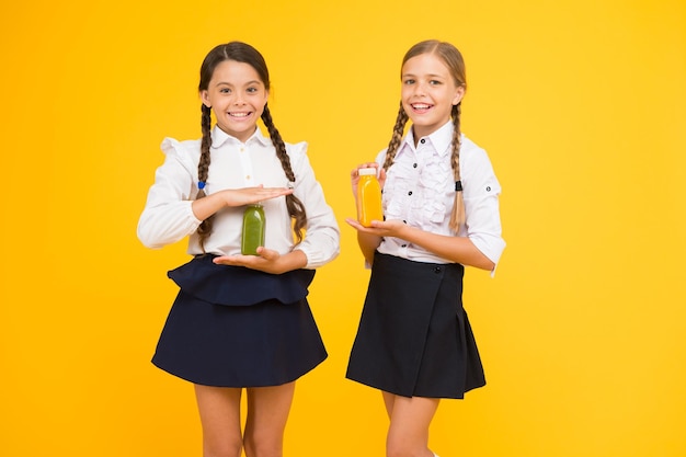 Succo di frutta fonte di energia Pranzo scolastico Bambini felici bevono frullato Cibo sano Nutrizione vitaminica Frullato fresco Ragazze bambini che bevono succo d'arancia frullato fresco Studentesse a pranzo