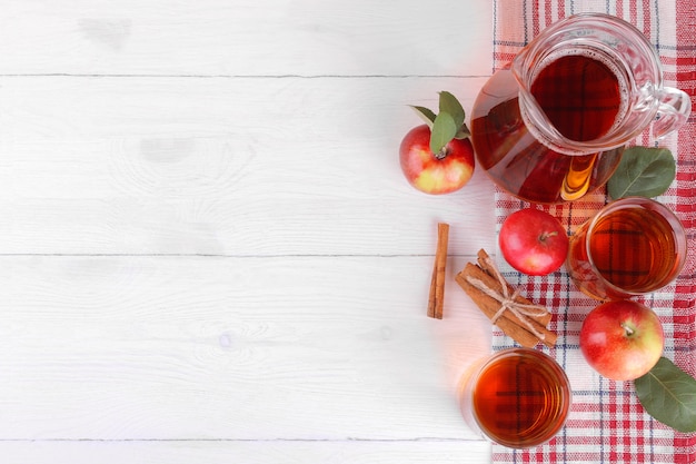 Succo di mela con mele fresche e cannella su un fondo di legno bianco