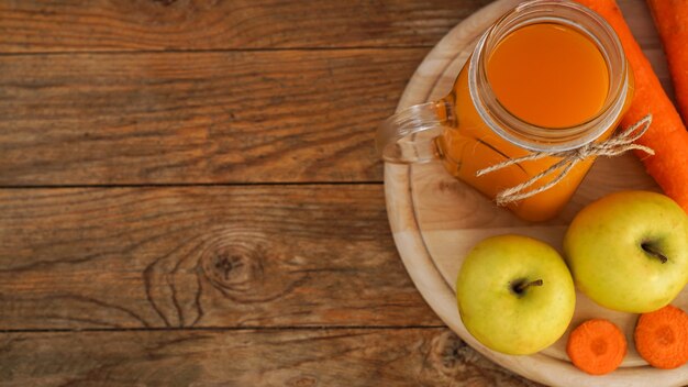 Succo di mela e carota in vetro, verdure fresche e frutta su fondo di legno. Stile rustico. Bevanda fatta in casa con vitamine