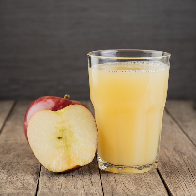 Succo di mela rossa in un bicchiere con frutta su un tavolo di legno