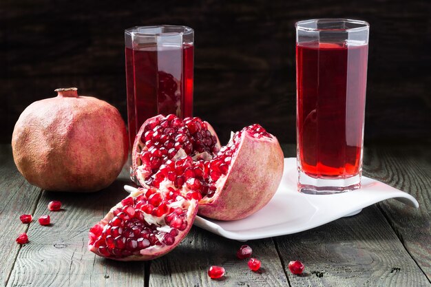 Succo di melograno in vetro e fette di melograno maturo con grani su tavola di legno