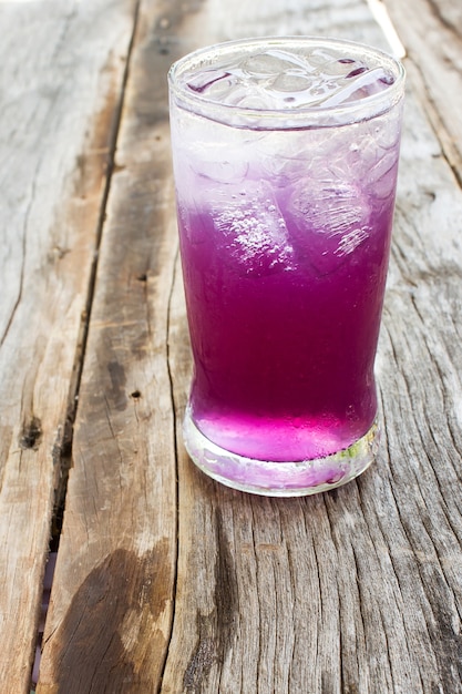 Succo di pisello di farfalla con limone e ghiaccio in vetro sul tavolo di legno.