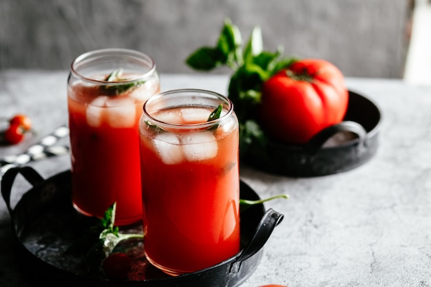 Succo di pomodoro con ghiaccio in un bicchiere su sfondo grigio