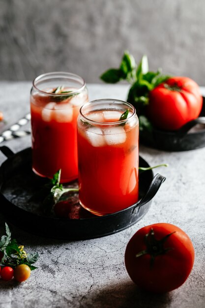 Succo di pomodoro con ghiaccio in un bicchiere su sfondo grigio