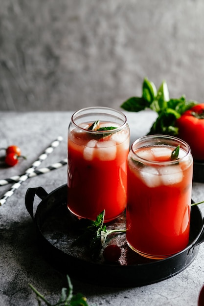 Succo di pomodoro con ghiaccio in un bicchiere su sfondo grigio