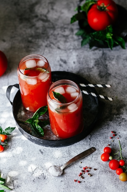 Succo di pomodoro con ghiaccio in un bicchiere su sfondo grigio