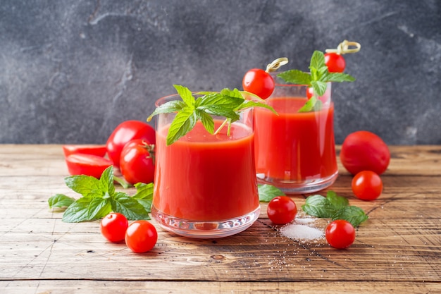 Succo di pomodoro con la menta in vetro e pomodori freschi su una tavola di legno. Concetto di alimenti biologici sani.