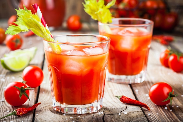 Succo di pomodoro con sedano e ghiaccio in bicchieri su un tavolo di legno