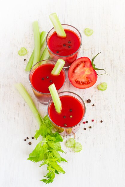 Succo di pomodoro con sedano e spezie su sfondo bianco.