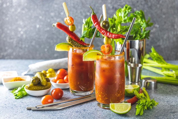 Succo di pomodoro con spezie di sedano sale e ghiaccio in bicchieri porzionati con spazio copia Cocktail Bloody Mary Bevanda alcolica e ingredienti sulla superficie del tavolo di cemento grigio