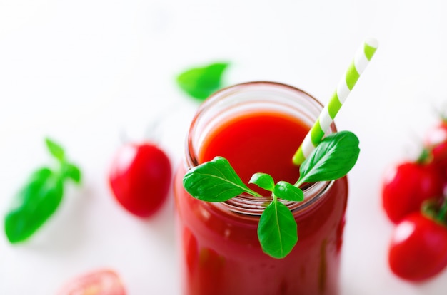 Succo di pomodoro fresco biologico in un vaso di vetro, basilico, ciliegia, sale, pepe e paglia sulla luce. Pulire il mangiare e il concetto di dieta.