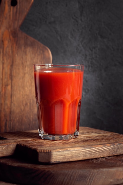 Succo di pomodoro fresco in vetro con cannuccia su tavola di legno vecchio su tavola rustica grigia