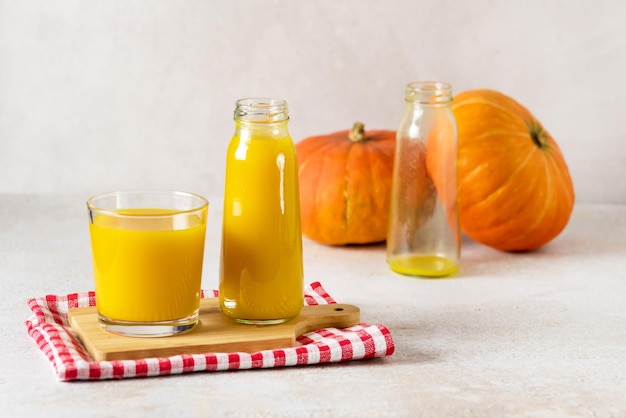 Succo di zucca appena spremuto in bottiglia di vetro con succo giallo sul tovagliolo vassoio in legno