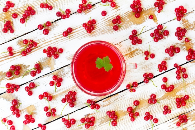 Succo rosso appena spremuto con ribes verde foglia e grappoli di ribes rosso su un tavolo in legno bianco con vecchio paintt.