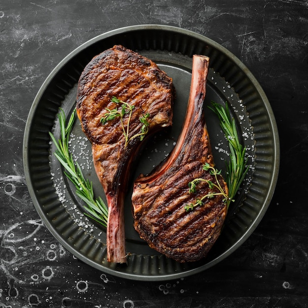 Succosa bistecca alla griglia con osso con spezie ed erbe aromatiche su uno sfondo di pietra nera Vista dall'alto Spazio per la copia gratuito