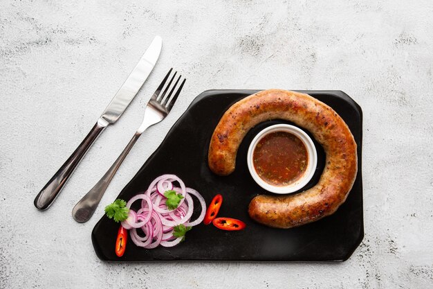 Succosa salsiccia al forno fatta in casa su un piatto con salsa piccante e cipolla marinata su fondo di marmo