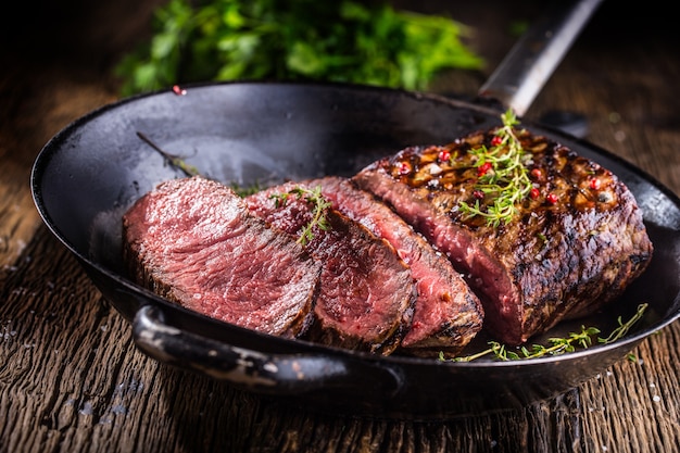 Succose fette di bistecca di manzo di manzo medio su tavola di legno con forchetta e coltello erbe spezie e sale