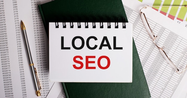 Sul desktop ci sono report, occhiali, una penna, un diario verde e un taccuino bianco con le parole LOCAL SEO