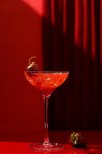 Sul tavolo c'è un cocktail rosso con fragole in un bicchiere. Una tenda rossa e un tavolo rosso.