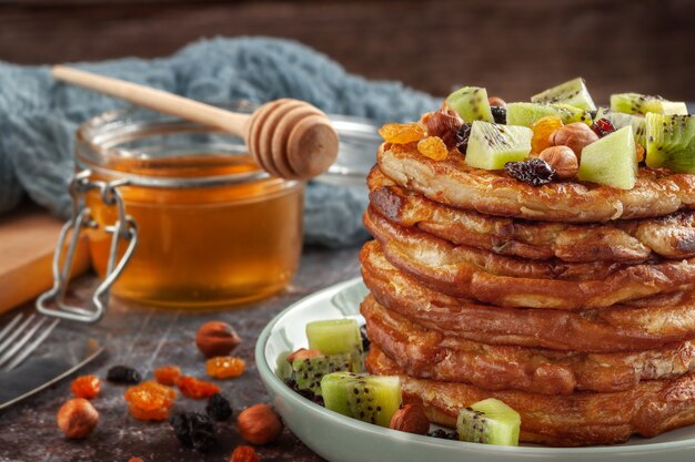 Sul tavolo c'è un piatto con frittelle, miele, kiwi, noci e uvetta