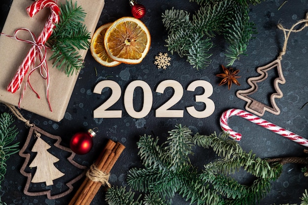 Sul tavolo c'è un regalo circondato da rami di alberi di Natale giocattoli di legno spezie e numeri 2023