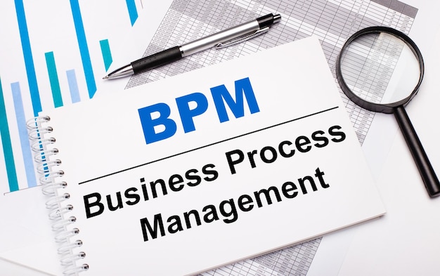 Sul tavolo report, diagrammi, una penna, una lente di ingrandimento e un blocco note bianco con BPM Business Process Management. concetto di business